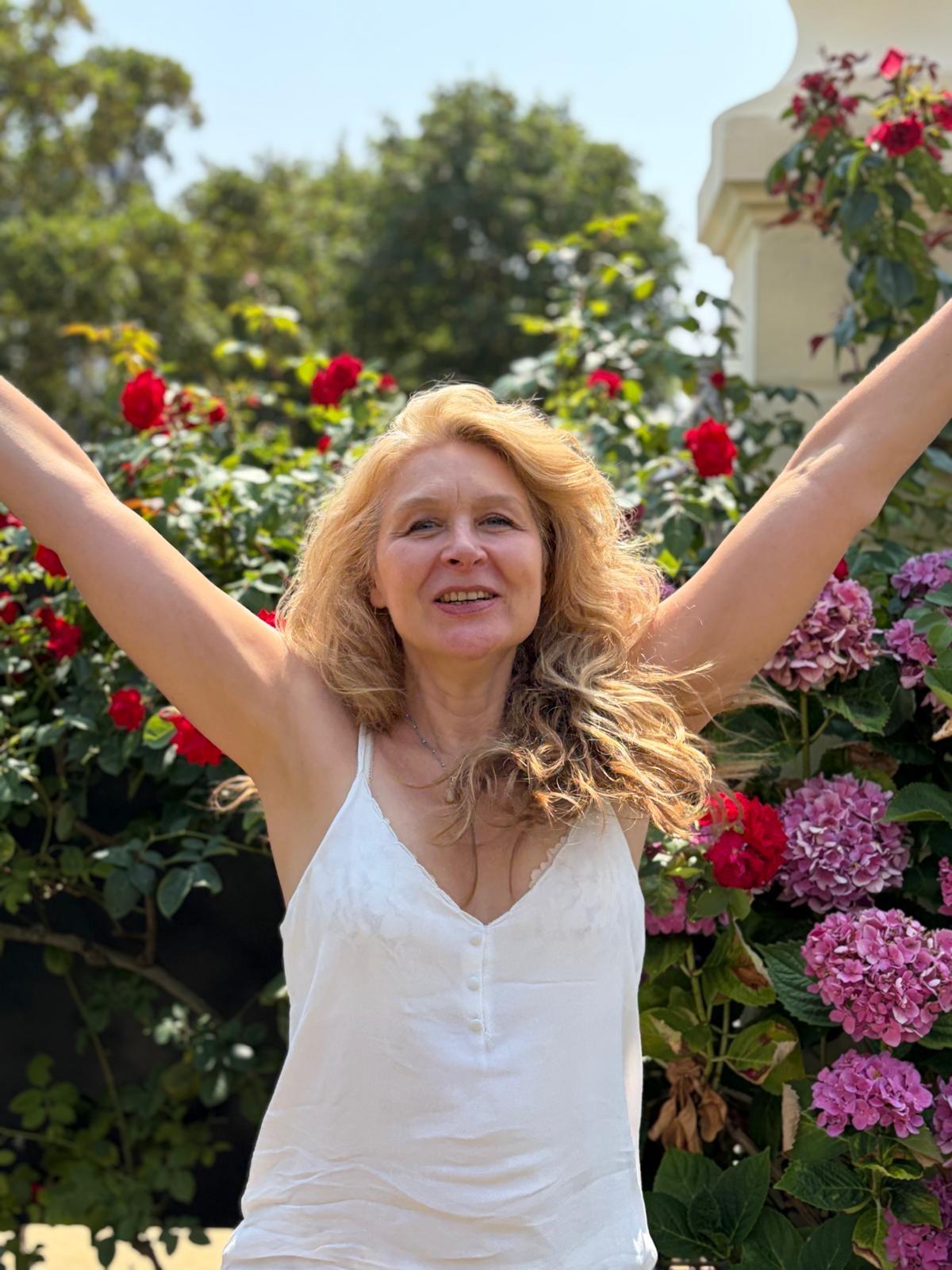 Alice Monnet Bertrand, facilitatrice de Biodanza, bras levés devant un jardin fleuri